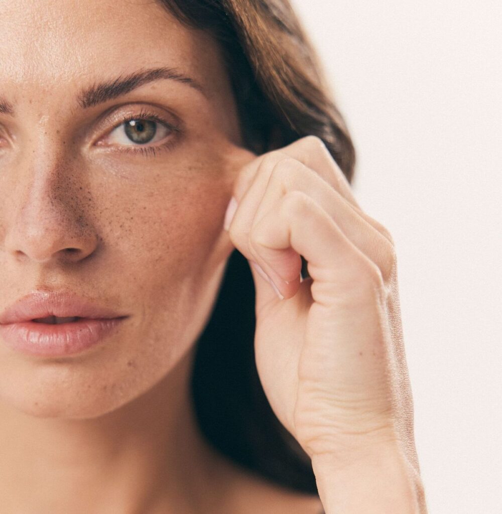 Mulher adulta tocando suavemente a lateral do rosto, em conteúdo sobre lifting Deep Plane e rejuvenescimento facial.